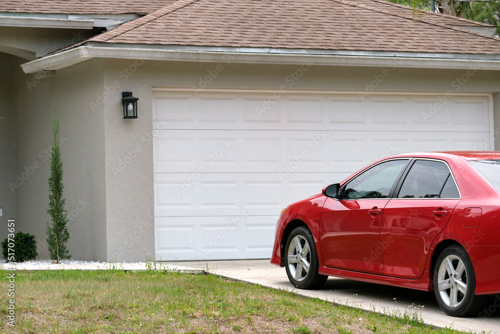 Car parked in front of wide garage double door on concrete driveway of new modern american house. Home and car security Rochester