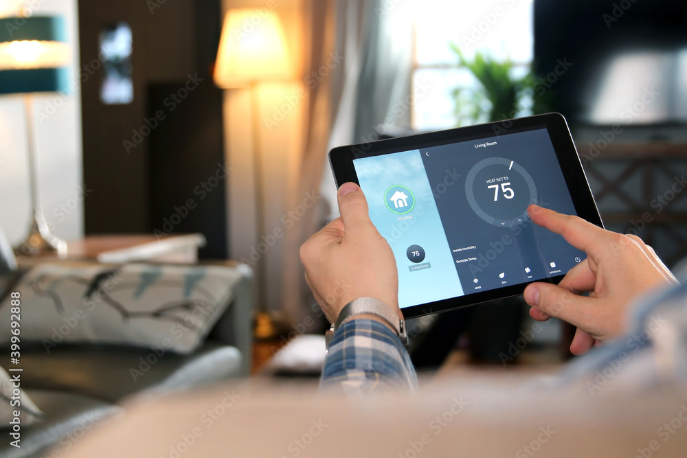 Man is Adjusting a temperature using a tablet with smart home app in modern living room. Smart home automation