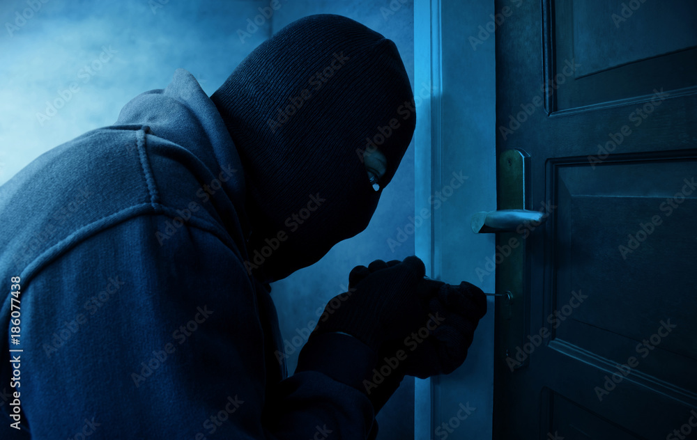 Masked thief using lock picker to open locked door