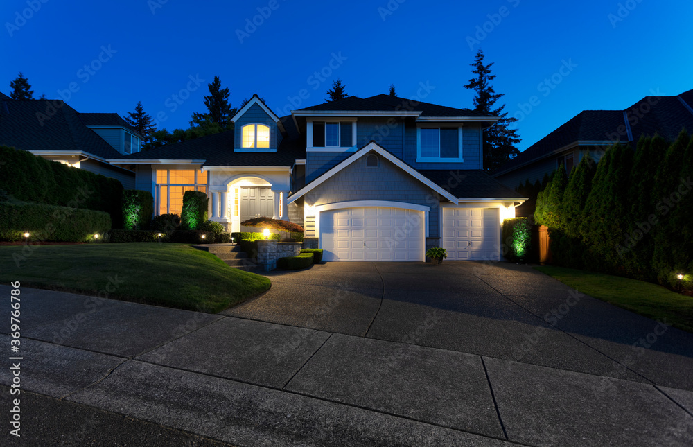 Suburban home exterior on a summer late evening with lights on yard and house. Home security