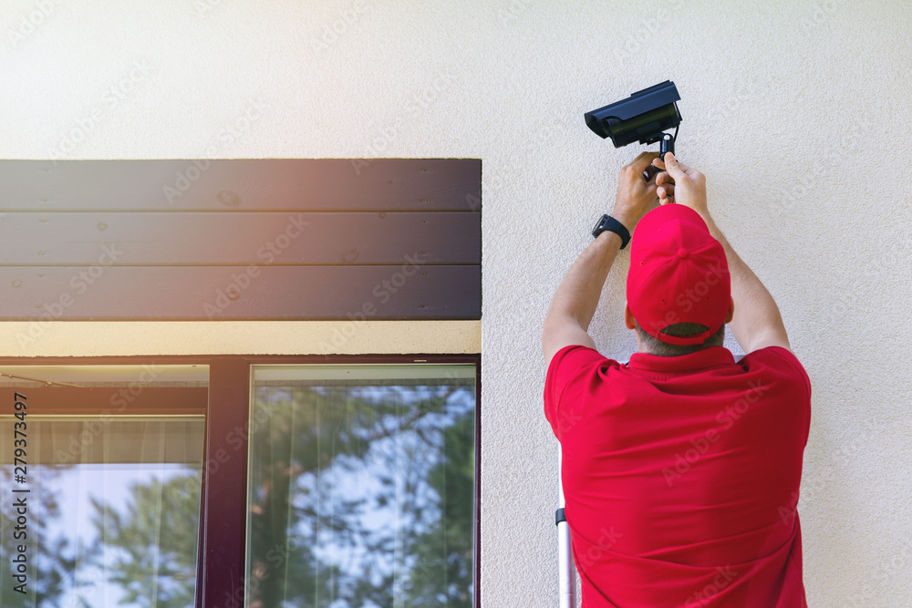 technician installing outdoor security surveillance camera on house exterior wall. Wireless home security