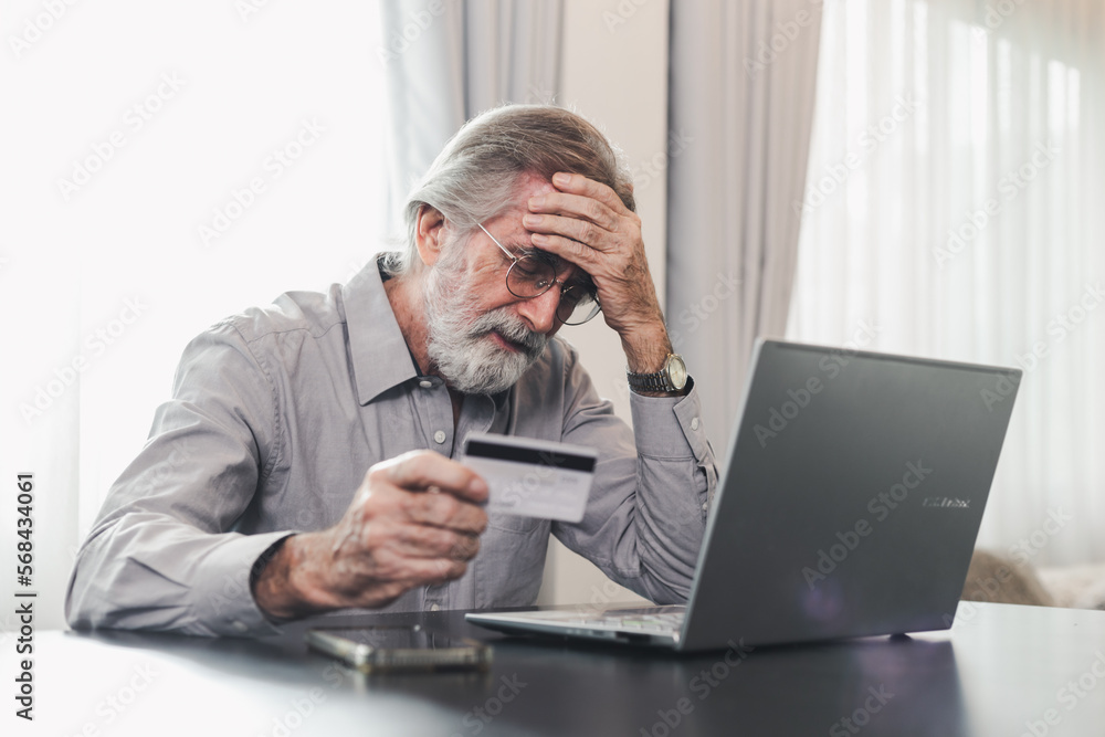 Upset senior elderly man holding credit card by laptop having trouble worry finance safety data or online payment security. Bank client concerned about problem with credit card, financial fraud threat. bank scams