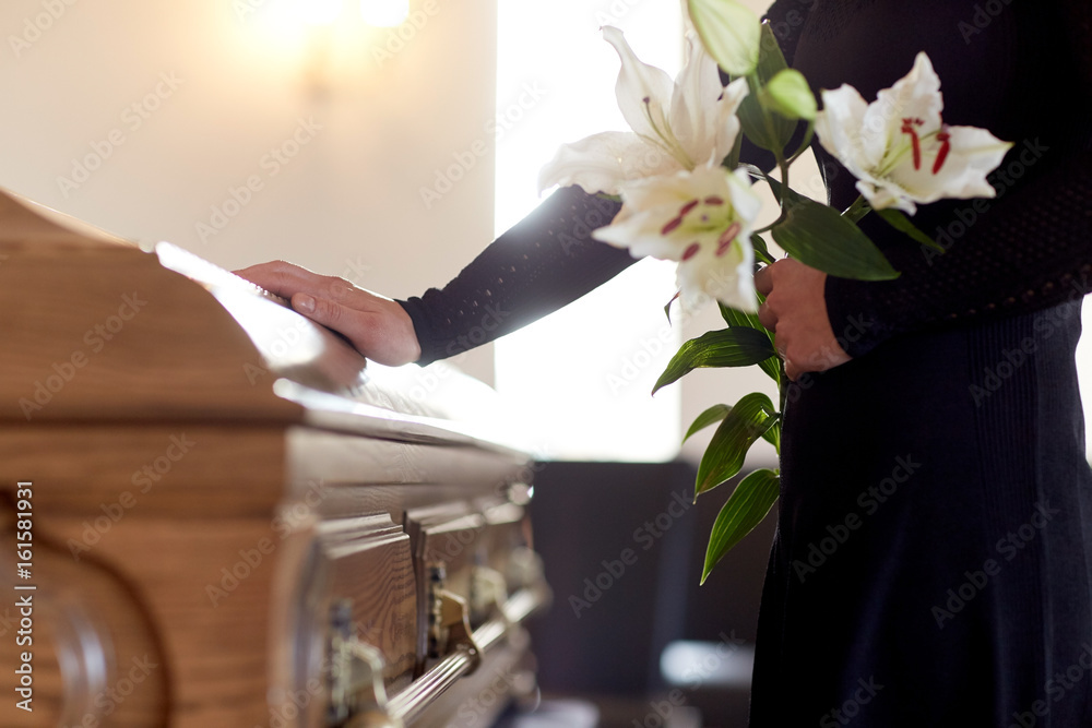 woman with lily flowers and coffin at funeral. Funeral burglary while your away.