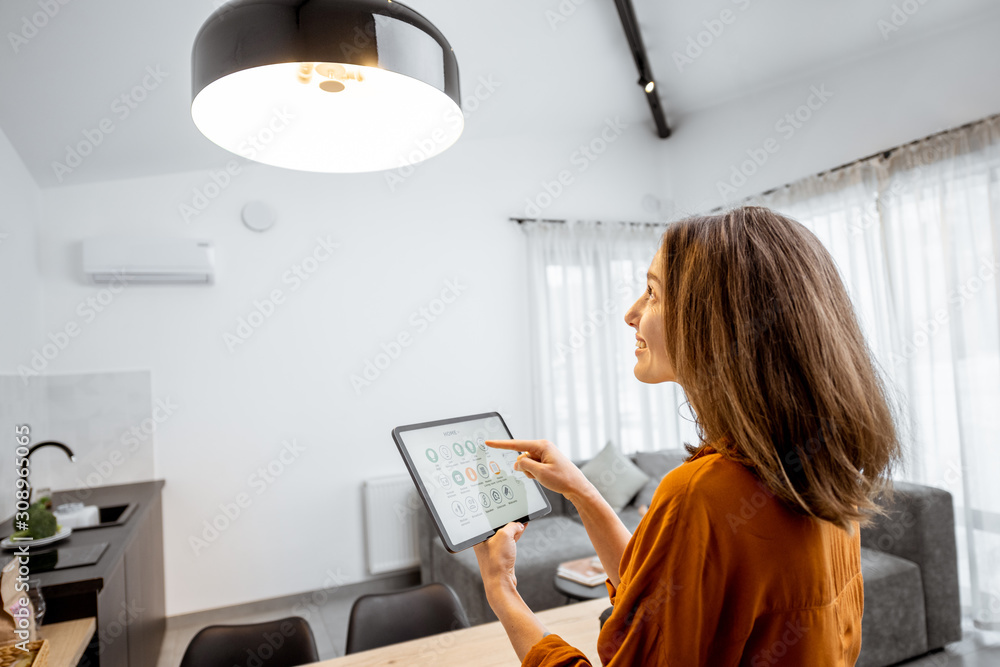 Young woman controlling home light with a digital tablet in the living room. Concept of a smart home and light control with mobile devices. Home automation