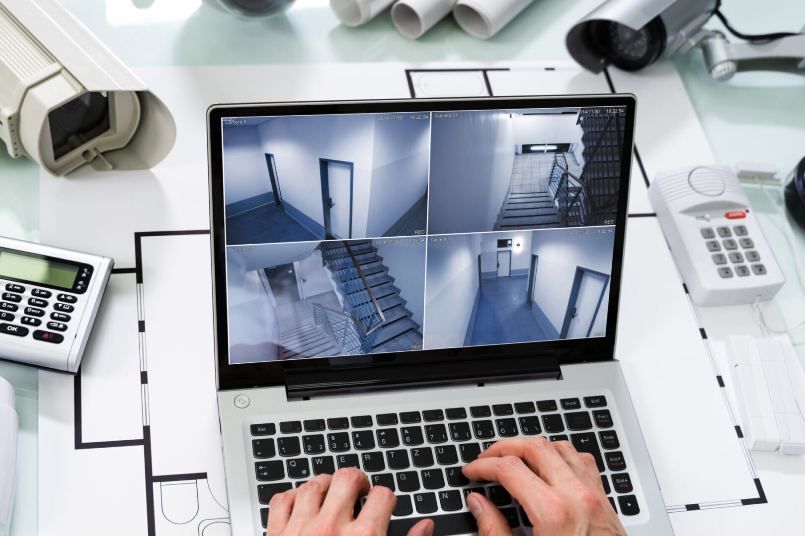 Hands typing on laptop with CCTV display