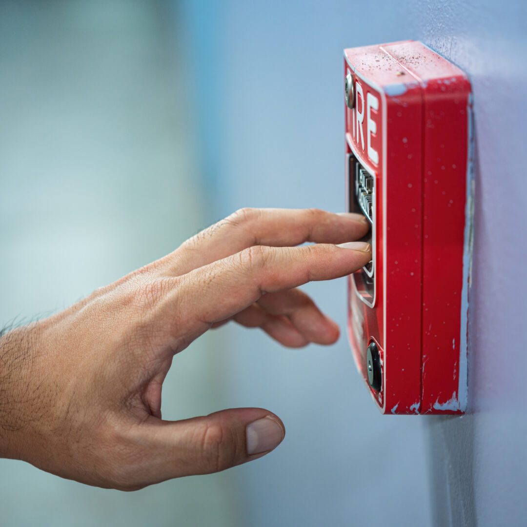 Hand pressing red fire alarm button