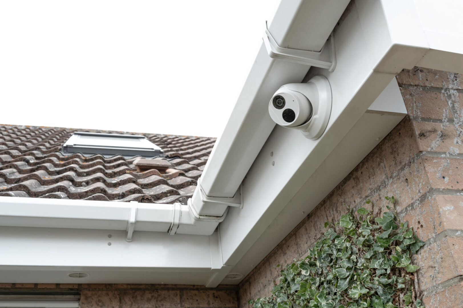 A white security camera mounted on a house gutter.