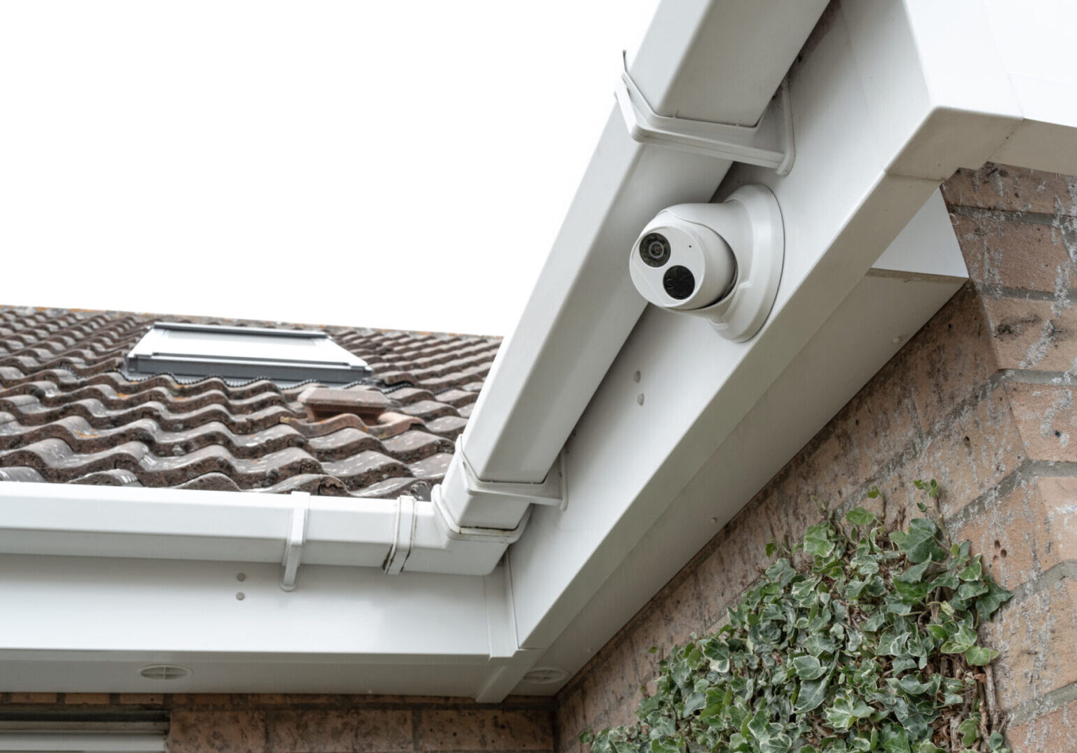 A white security camera mounted on a house gutter.